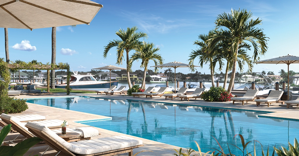 Waterfront resort pool with palm trees, loungers, umbrellas, and marina views