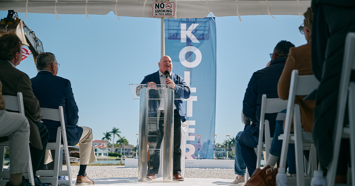 Speaker addresses seated audience at a tented groundbreaking ceremony.