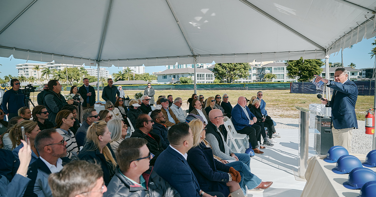 Audience listens to speaker under a tent at a waterfront groundbreaking.