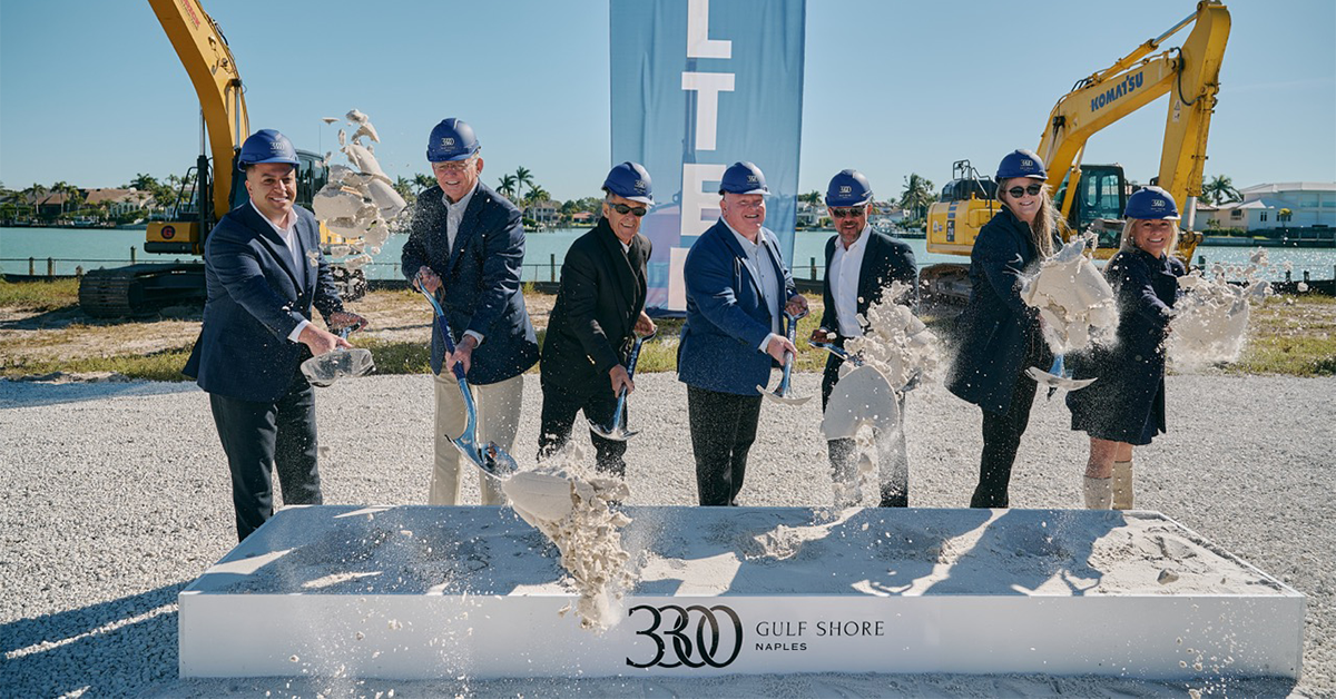 Executives in blue hard hats shovel concrete at a Kolt Naples groundbreaking ceremony.
