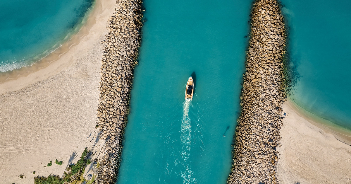 Aerial view of boat traveling between rock jetties into turquoise Gulf waters near Naples Florida