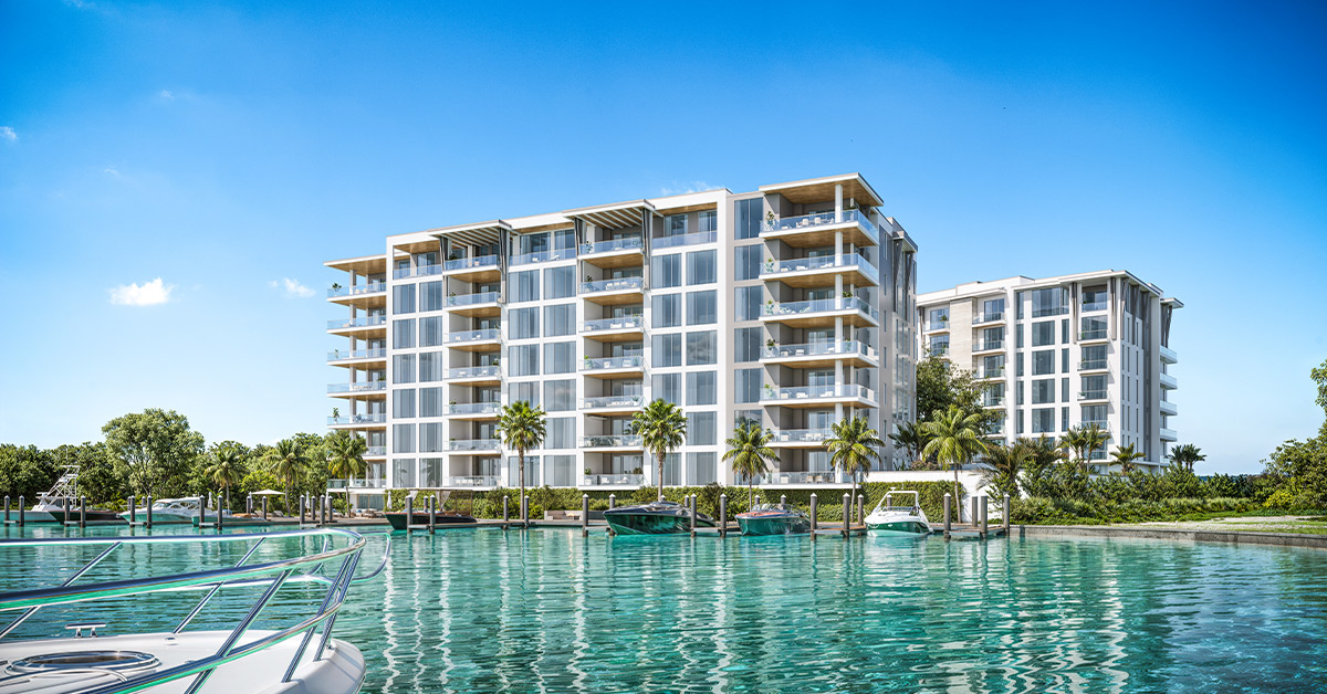 Waterfront condo building with marina, boats, and palm trees under blue sky.